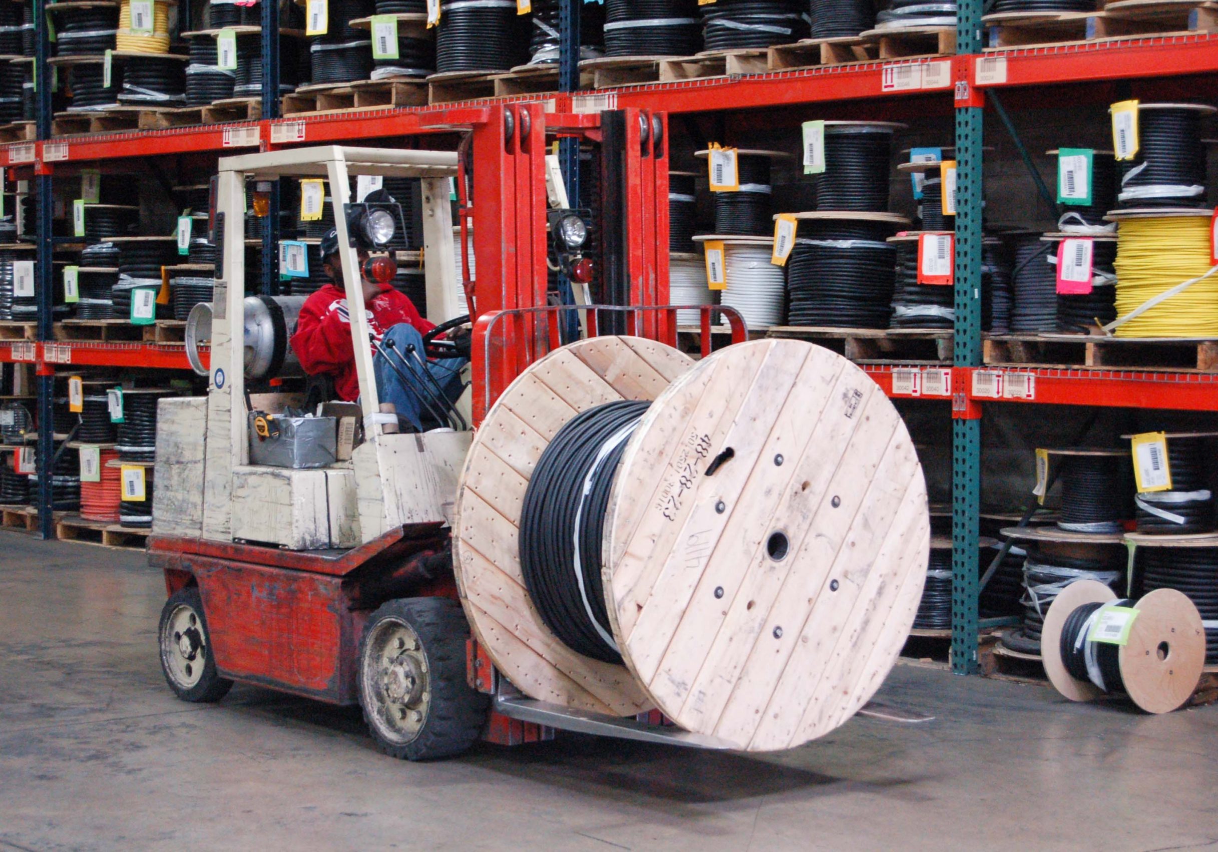 A reel of wire being transported in a warehouse via forklift.
